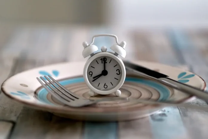 Weißer Wecker auf einem Teller mit Besteck – symbolisiert zeitbeschränktes Essen beim Intervallfasten.