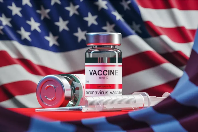 COVID-19-Impfstofffläschchen und Spritze im Vordergrund vor einer wehenden US-Flagge
