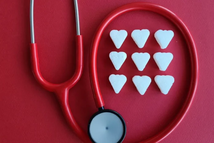 Rotes Stethoskop liegt auf rotem Hintergrund neben neun weißen, herzförmigen Zuckerstücken.