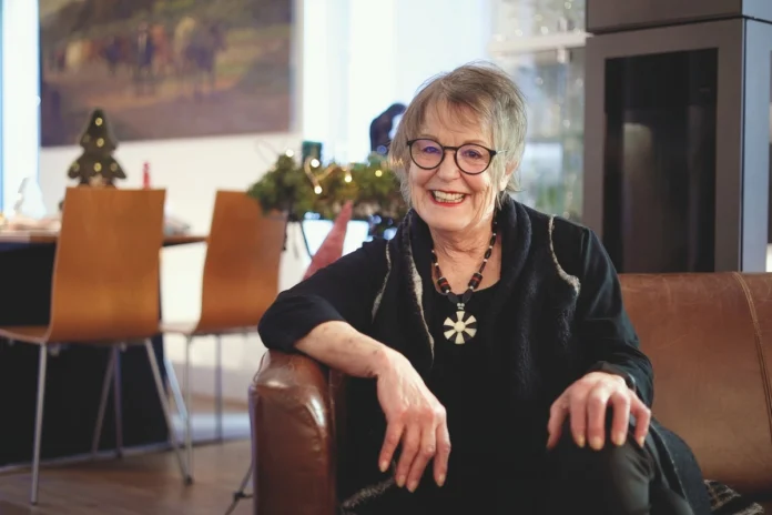 Frau Schmid, Überlebende eines plötzlichen Herzstillstands, sitzt lächelnd in ihrem Wohnzimmer