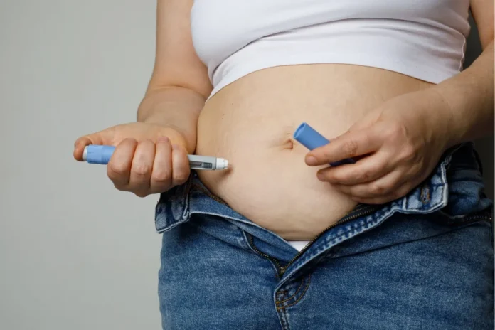 Person setzt sich mit einem Medikamenten-Pen eine Injektion in den Bauch.