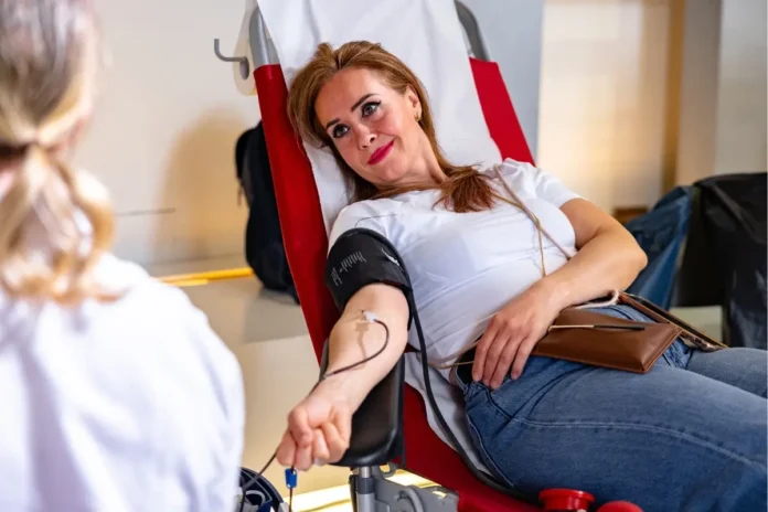 Eine Frau liegt entspannt auf einem Spenderstuhl und spendet Blut, während medizinisches Personal neben ihr sitzt.
