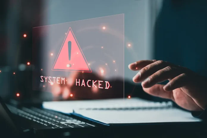 Warnhinweis „System hacked“ auf einem Bildschirm vor einer Person am Laptop.