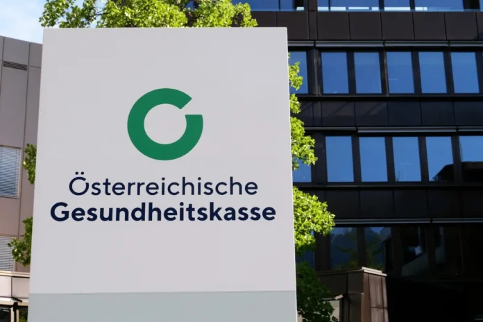 Schild mit dem Logo und dem Schriftzug „Österreichische Gesundheitskasse“ vor einem modernen Bürogebäude.