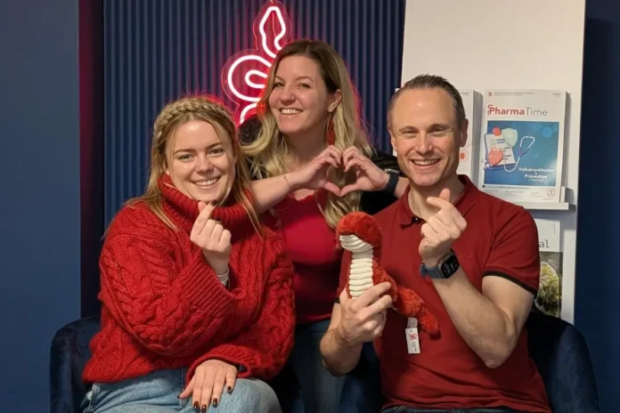 Drei Personen vor einem blauen Hintergrund tragen rote Kleidung und zeigen mit den Händen Herzsymbole