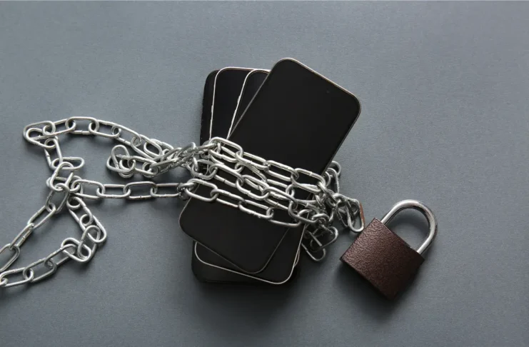 Mehrere Smartphones sind mit einer Metallkette umwickelt und mit einem Vorhängeschloss gesichert.