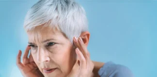 ltere Frau mit kurzen grauen Haaren hält sich konzentriert die Schläfen, möglicherweise wegen Ohrgeräuschen oder Kopfschmerzen.