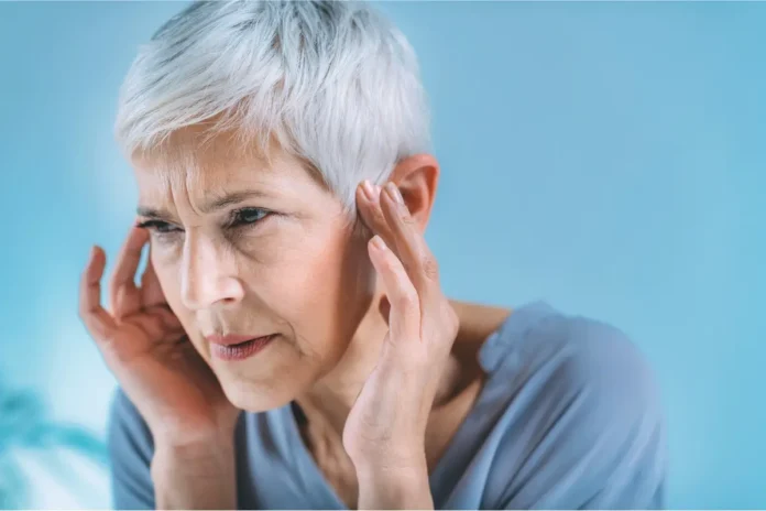 ltere Frau mit kurzen grauen Haaren hält sich konzentriert die Schläfen, möglicherweise wegen Ohrgeräuschen oder Kopfschmerzen.