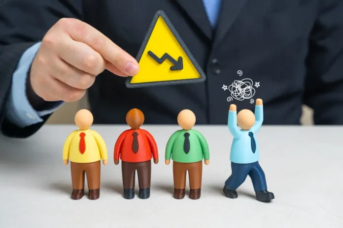 Hand eines Geschäftsmanns hält ein gelbes Warnschild mit fallendem Pfeil über vier Figuren; eine Figur wirkt gestresst und hebt die Arme.