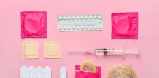 Verschiedene Verhütungsmittel und medizinische Produkte auf rosa Hintergrund, darunter Kondome in Verpackungen, eine Antibabypillen-Blisterpackung, eine Spritze, Pflaster und Vaginalzäpfchen.