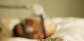 Eine Person liegt im Bett und wird mit einem Beatmungsgerät beatmet.