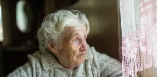 Ältere Frau sitzt allein am Fenster und blickt nach draußen – Symbolbild für Alterseinsamkeit