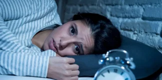 Frau liegt wach im Bett neben Wecker und wirkt erschöpft trotz Schlafproblemen