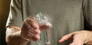 and mit zitternder Bewegung hält ein Glas Wasser – typisches Symptom bei Parkinson Erkrankung