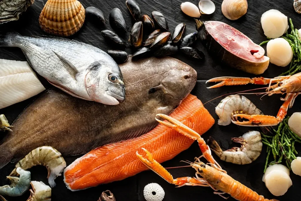 Verschiedene Fischarten und Meeresfrüchte wie Lachs, Muscheln und Garnelen auf dunklem Untergrund
