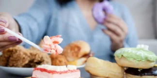 Frau sitzt vor Süßspeisen und Fast Food als Symbolbild für Essstörungen und problematisches Essverhalten