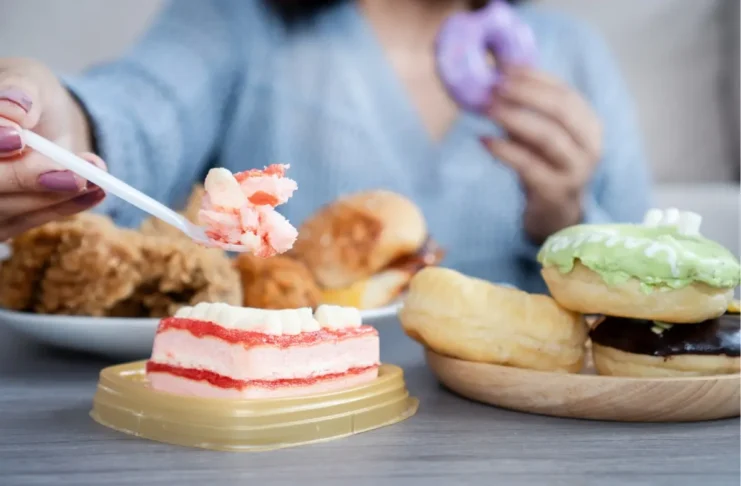 Frau sitzt vor Süßspeisen und Fast Food als Symbolbild für Essstörungen und problematisches Essverhalten