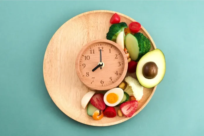 Teller mit Uhr und Lebensmitteln als Symbol für ein frühes Abendessen und verlängertes nächtliches Fasten