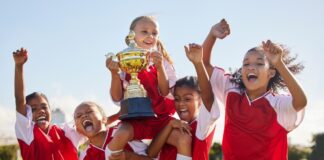 Kinder feiern nach einem Sportbewerb mit einem Pokal. Regelmäßige Bewegung kann die psychische Gesundheit von Kindern und Jugendlichen fördern.