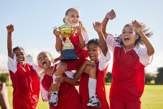 Kinder feiern nach einem Sportbewerb mit einem Pokal. Regelmäßige Bewegung kann die psychische Gesundheit von Kindern und Jugendlichen fördern.