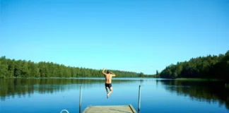 Person springt an einem heißen Sommertag von einem Badesteg in einen See.