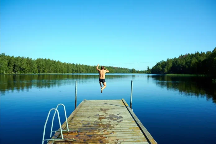 Person springt an einem heißen Sommertag von einem Badesteg in einen See.