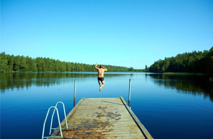 Person springt an einem heißen Sommertag von einem Badesteg in einen See.