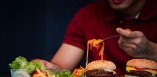 Person isst Burger und Pommes – Symbolbild für gestörte Hunger- und Sättigungsregulation bei hypothalamischer Adipositas.