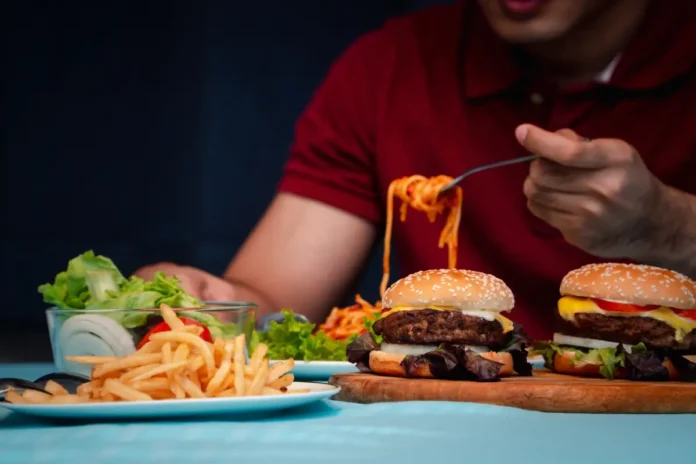Person isst Burger und Pommes – Symbolbild für gestörte Hunger- und Sättigungsregulation bei hypothalamischer Adipositas.