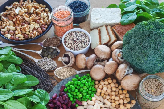 Pflanzliche und tierische Proteinquellen wie Hülsenfrüchte, Nüsse, Tofu, Brokkoli und Pilze auf einem Tisch.