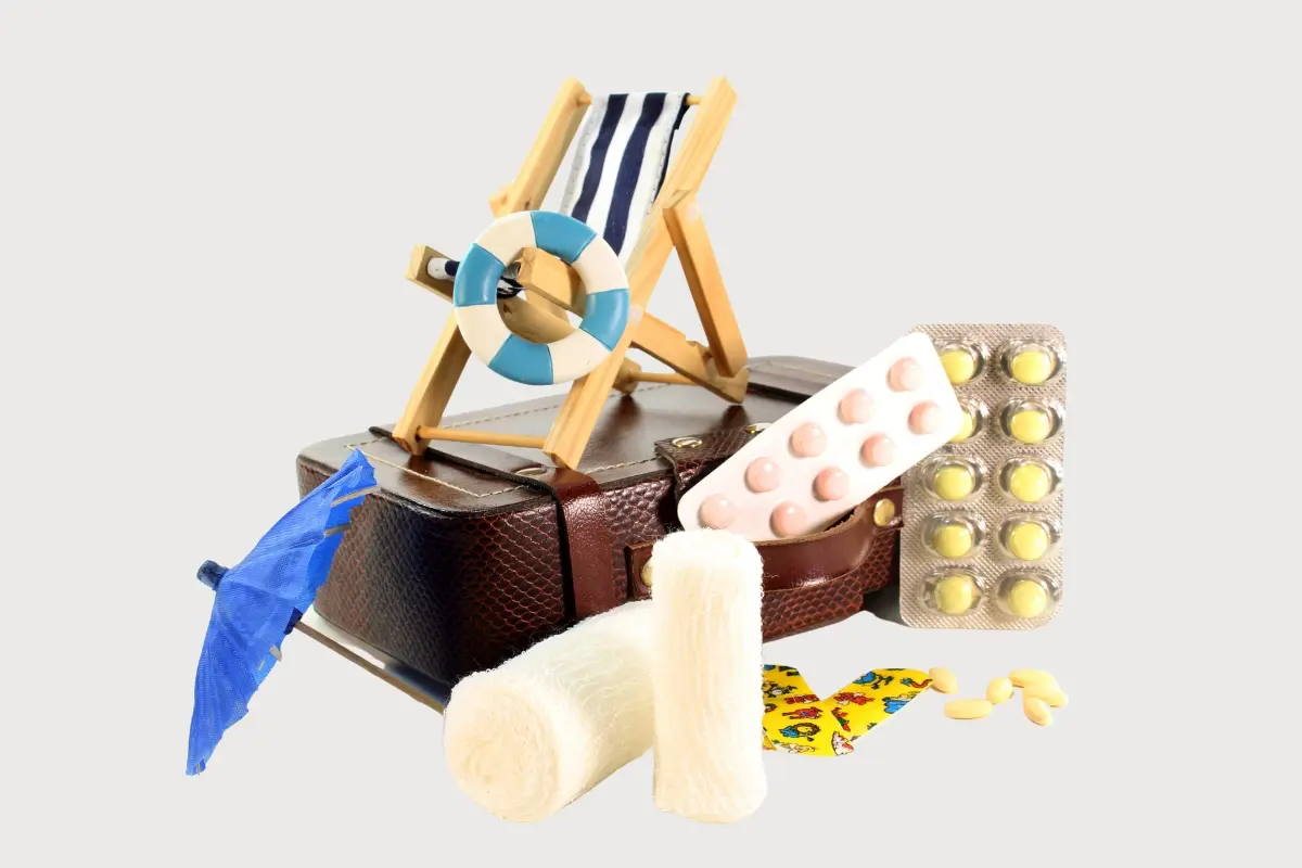 Koffer mit Reiseapotheke, Medikamenten und Symbolen für Urlaub und Krankenversicherung im Ausland.