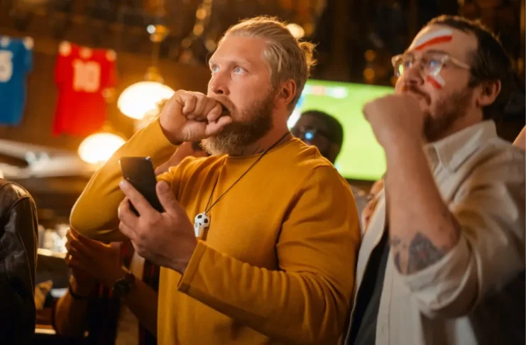 Fans verfolgen ein Fußballspiel in einem Lokal. Suchtexperten warnen, dass Sportwetten während großer Turniere problematisches Wettverhalten verstärken können.