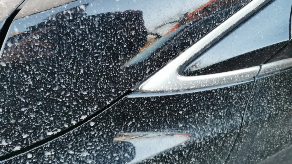 Feiner Wüstenstaub bedeckt die Motorhaube und den Scheinwerfer eines schwarzen Autos.