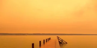 Wüstenstaub färbt den Himmel über einem See orange.