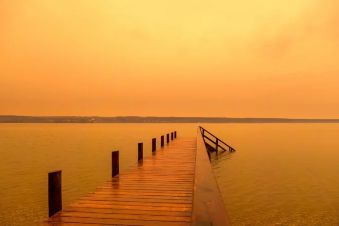 Wüstenstaub färbt den Himmel über einem See orange.