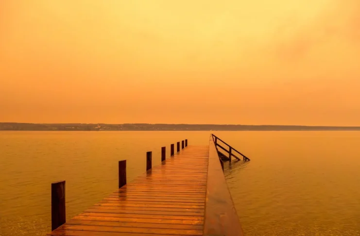 Wüstenstaub färbt den Himmel über einem See orange.