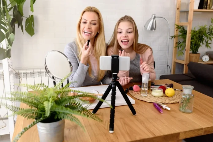Kosmetik bei Kindern und Jugendlichen: Junge Frau und Mädchen verwenden Kosmetik vor einer Smartphone-Kamera.