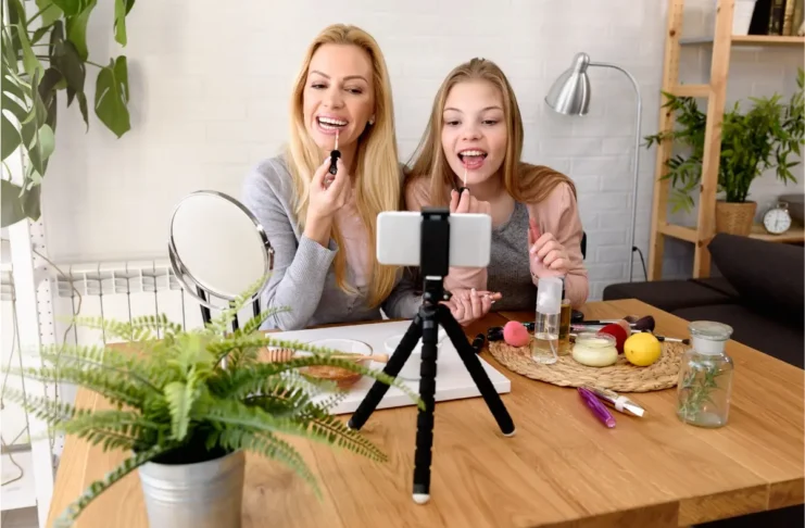 Kosmetik bei Kindern und Jugendlichen: Junge Frau und Mädchen verwenden Kosmetik vor einer Smartphone-Kamera.