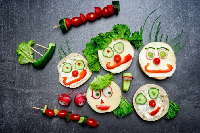 Gesichter aus Gemüse auf Broten und Gemüsespießen als Symbolbild für vegetarische und vegane Ernährung bei Kindern.