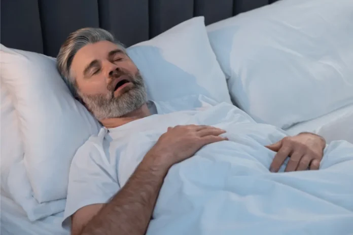 Schlafender Mann mit geöffnetem Mund im Bett als Symbolbild für obstruktive Schlafapnoe