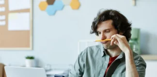 Mann blickt auf sein Smartphone, während vor ihm ein geöffneter Laptop steht.