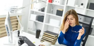 Frau am Computer reibt sich die Augen und hält ihre Brille in der Hand