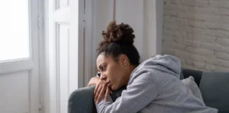Frau sitzt nachdenklich auf einem Sofa am Fenster