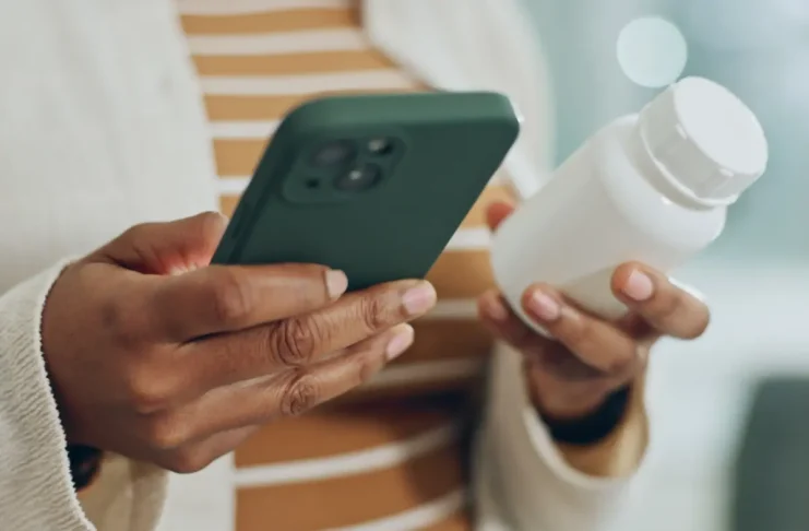 Person mit Smartphone und Medikamentenbehälter