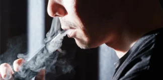Mann nutzt einen Tabakerhitzer und stößt eine sichtbare Aerosolwolke aus.