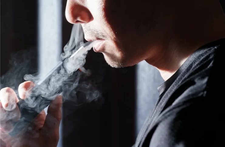 Mann nutzt einen Tabakerhitzer und stößt eine sichtbare Aerosolwolke aus.