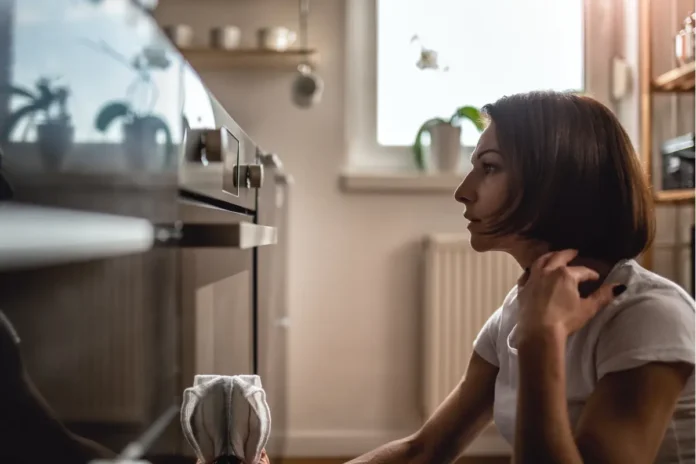 Frau sitzt vor einem Backofen in einer Küche – Symbolbild für Zwangsstörungen.