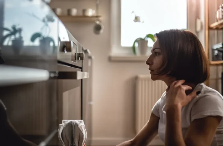Frau sitzt vor einem Backofen in einer Küche – Symbolbild für Zwangsstörungen.
